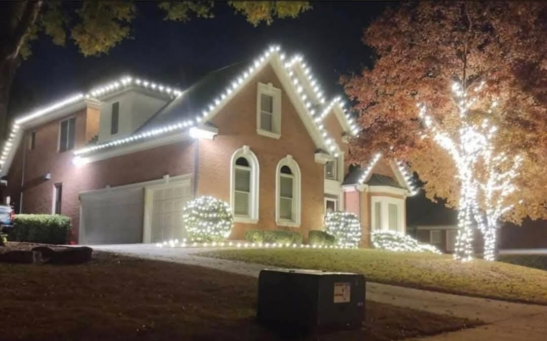 Brick home with roofline lights, shrub lights and a wrapped fall tree