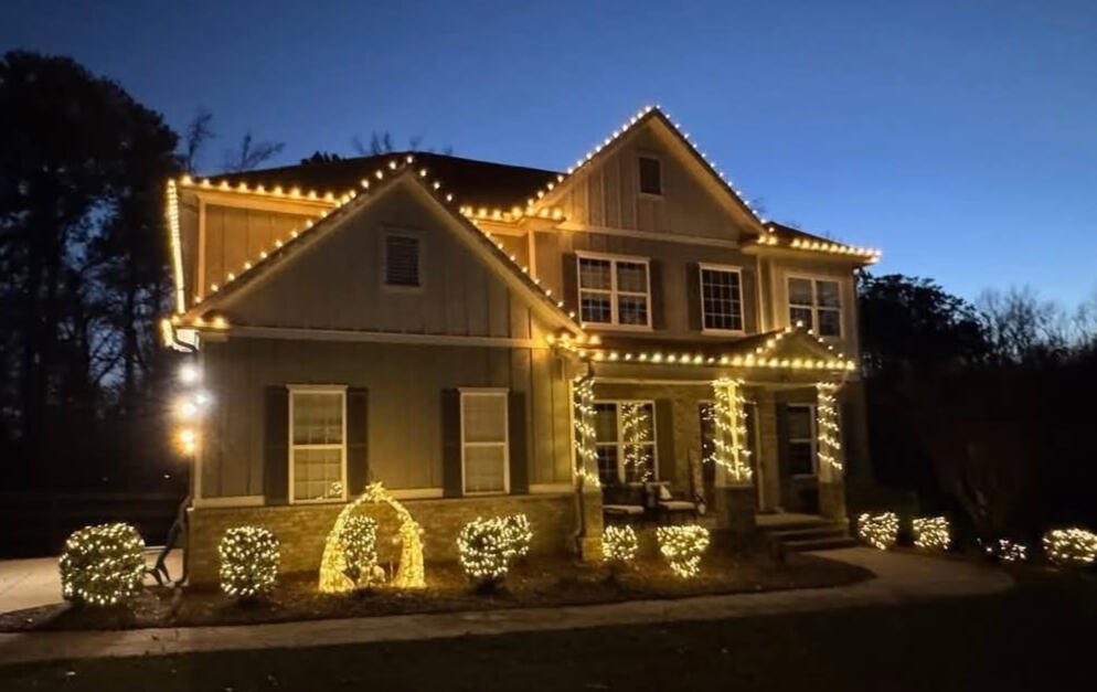 Farmhouse-style home with warm white roofline, column and shrub lighting