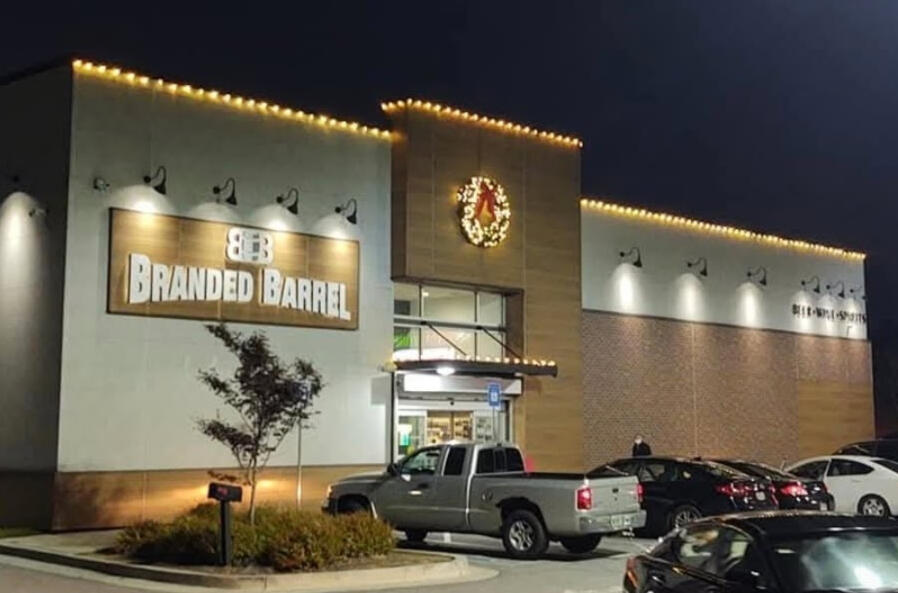 Commercial holiday lighting on a retail storefront roofline with a lit wreath at night