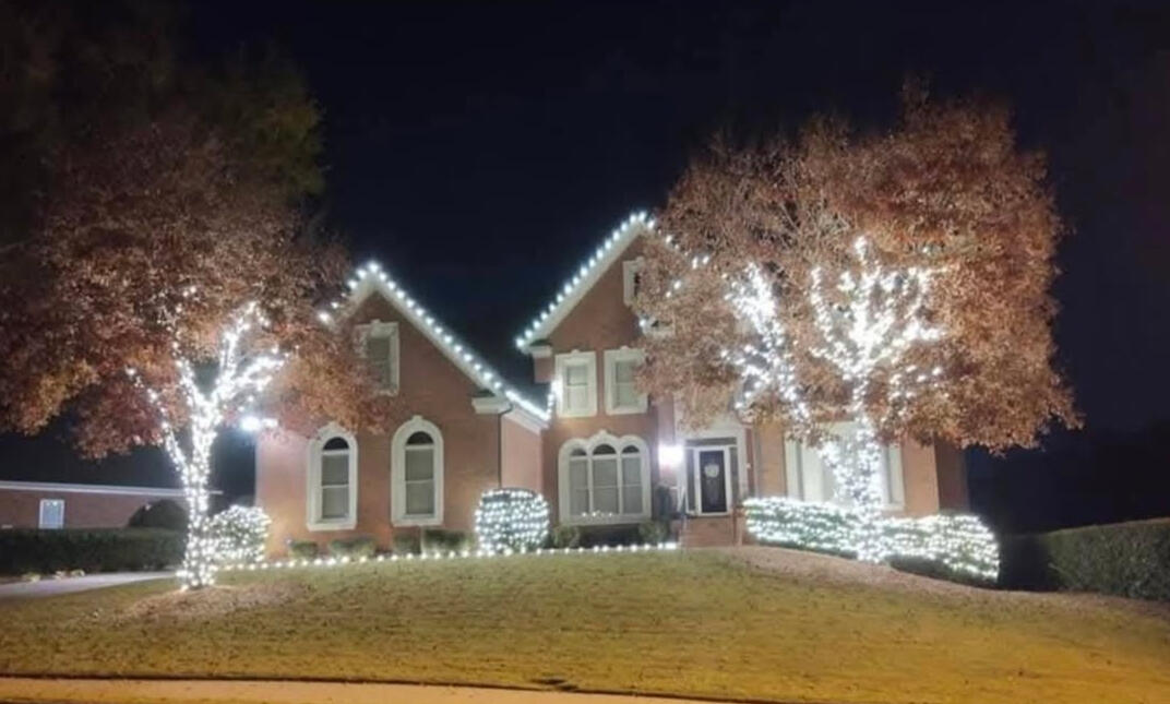Brick home on a hill with roofline lights and two wrapped trees
