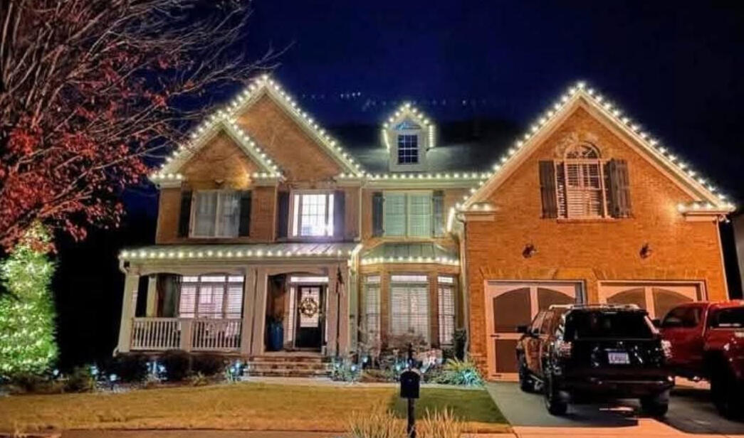 Brick two-story home with roofline Christmas lights and a lit evergreen