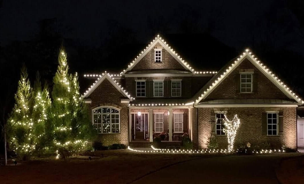 Brick home with roofline Christmas lights and wrapped evergreen trees